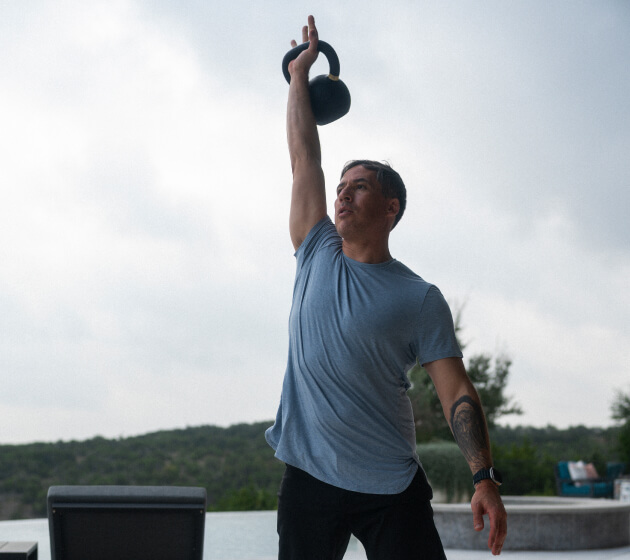 A person lifts a kettlebell overhead outdoors.