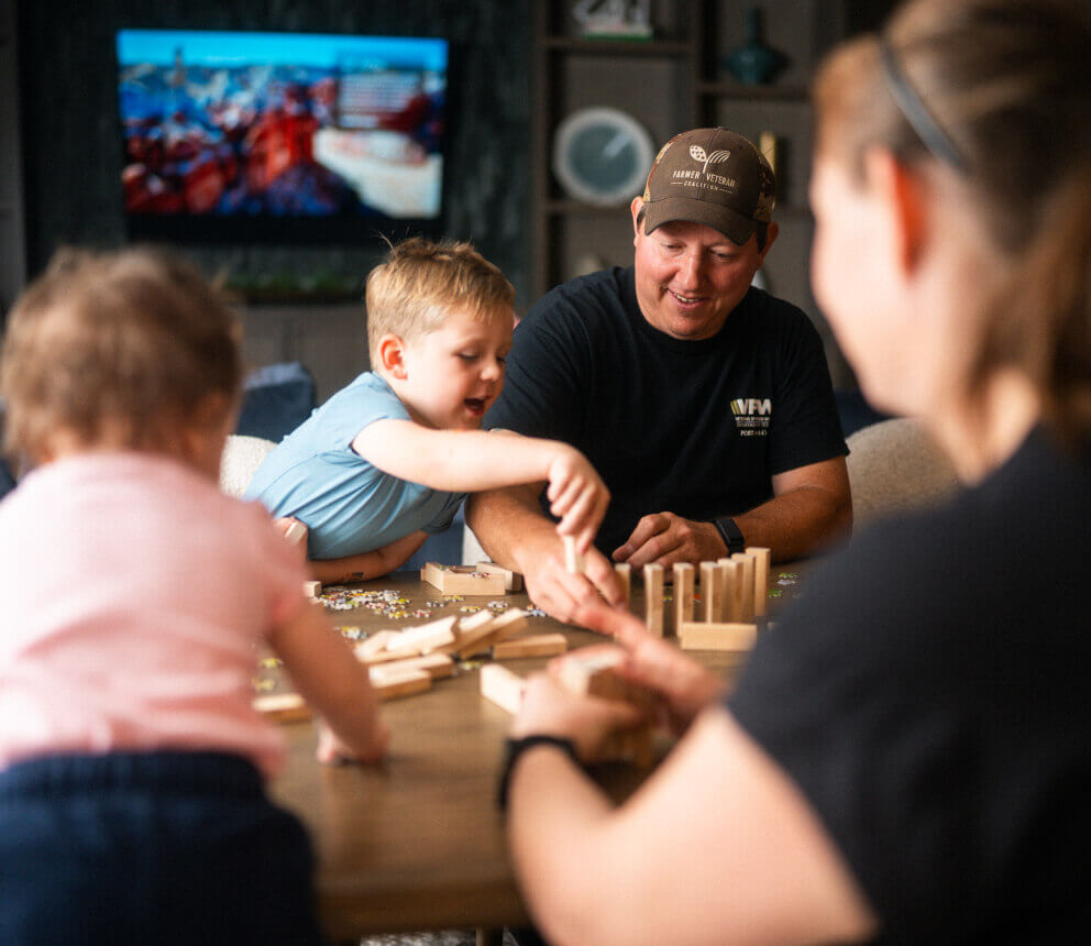 An adult and children sit at a table building with wooden blocks.