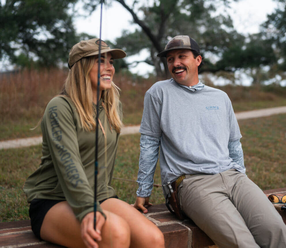 Two people sit outdoors talking, with fishing rods nearby.