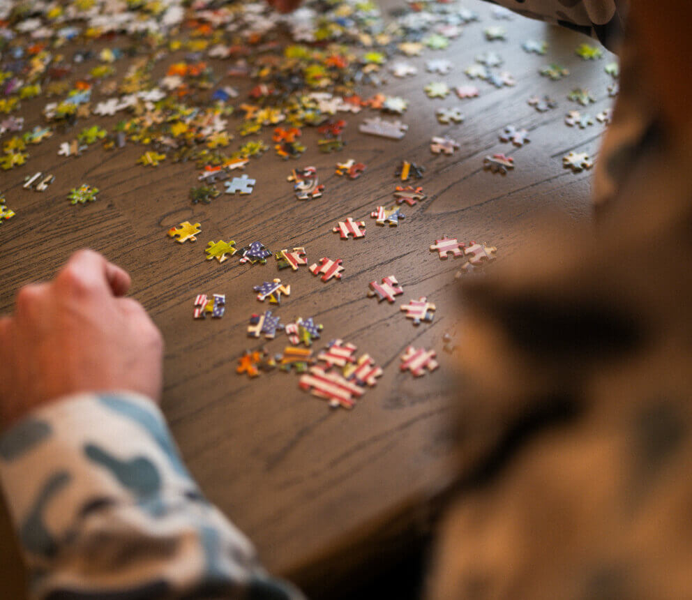 Puzzle pieces spread across a table as people work on a jigsaw puzzle.